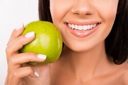 woman holding green apple next to her white teeth smiling, veneers in Beaver Dam, WI