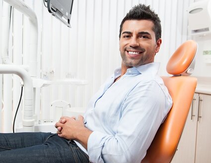 man sitting in orange dental exam chair smiling, getting dental implants Katy, TX dentist