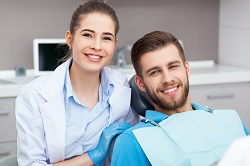 man in dental chair smiling, female assistant dentist