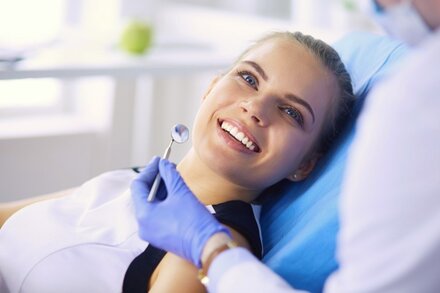 blond teen girl smiling wearing dental bib, dentist hand with tool near mouth, general dentist Old Bridge, NJ