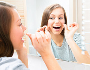 girl flossing her teeth in bathroom mirror, general dentistry Old Bridge, NJ dentist 08857